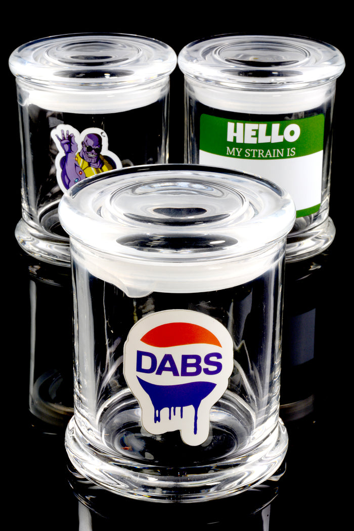Trio of large glass stash jars on glossy black surface featuring assorted decals—DABS logo, Thanos snap, blank strain label—illustrating random design