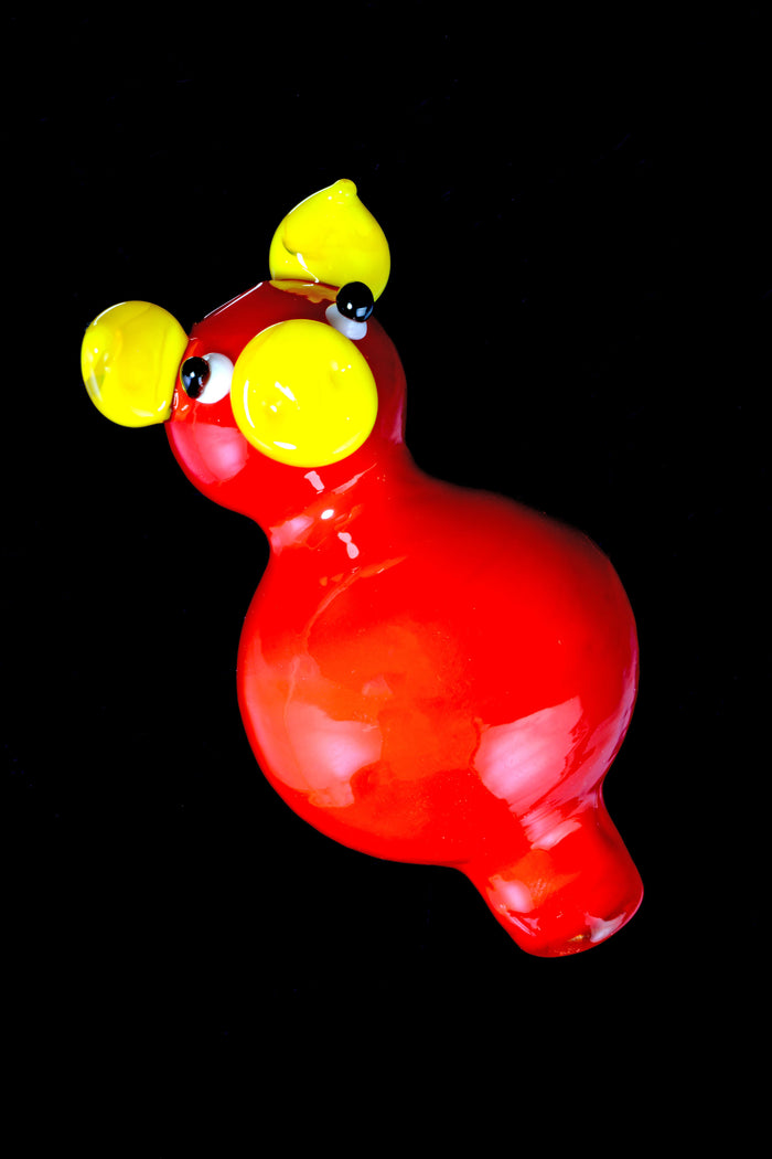 Closeup of glossy red glass pig bubble carb cap with yellow ears and snout, shown angled on a black background.