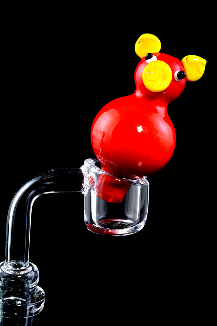 Pig-themed glass bubble carb cap seated on a flat-top quartz banger, angled to cap the bucket and control airflow.
