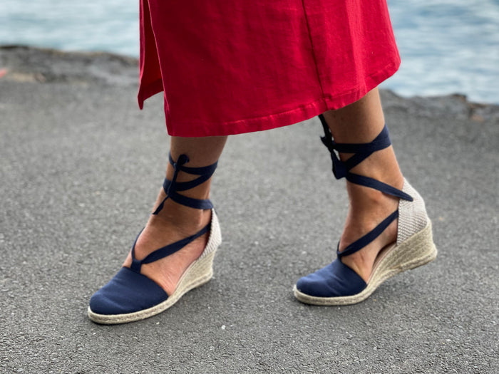 A person wearing Via Nova Flynn sandals in navy blue color. European Espadrille women's sandals with enclosed heel and toe. Woven wedge heel, lace up straps. Comfortable footbed. Made in Spain.