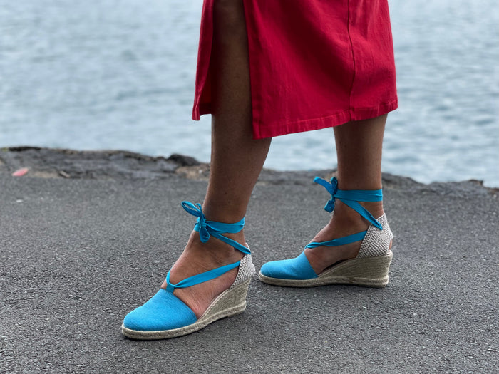 A person wearing Via Nova Flynn sandals in turquoise blue color. European Espadrille women's sandals with enclosed heel and toe. Woven wedge heel, lace up straps. Comfortable footbed. Made in Spain.