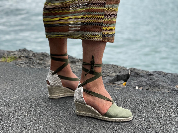 A person wearing Via Nova Flynn sandals in khaki green color. European Espadrille women's sandals with enclosed heel and toe. Woven wedge heel, lace up straps. Comfortable footbed. Made in Spain.