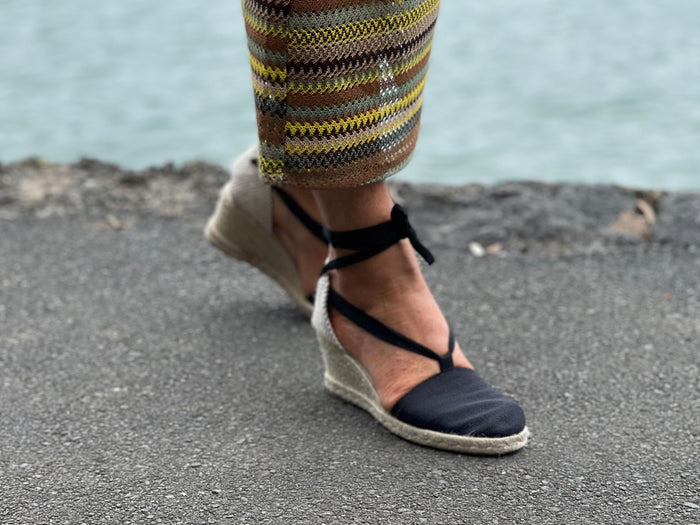 A person wearing Via Nova Flynn sandals in black color. European Espadrille women's sandals with enclosed heel and toe. Woven wedge heel, lace up straps. Comfortable footbed. Made in Spain.